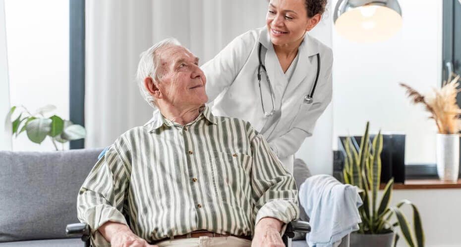 An elderly man in a wheelchair is being helped by a nurse.