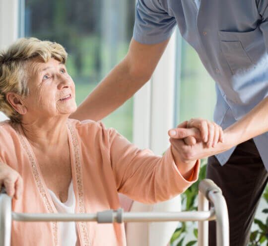 A man is helping an elderly woman with a walker.