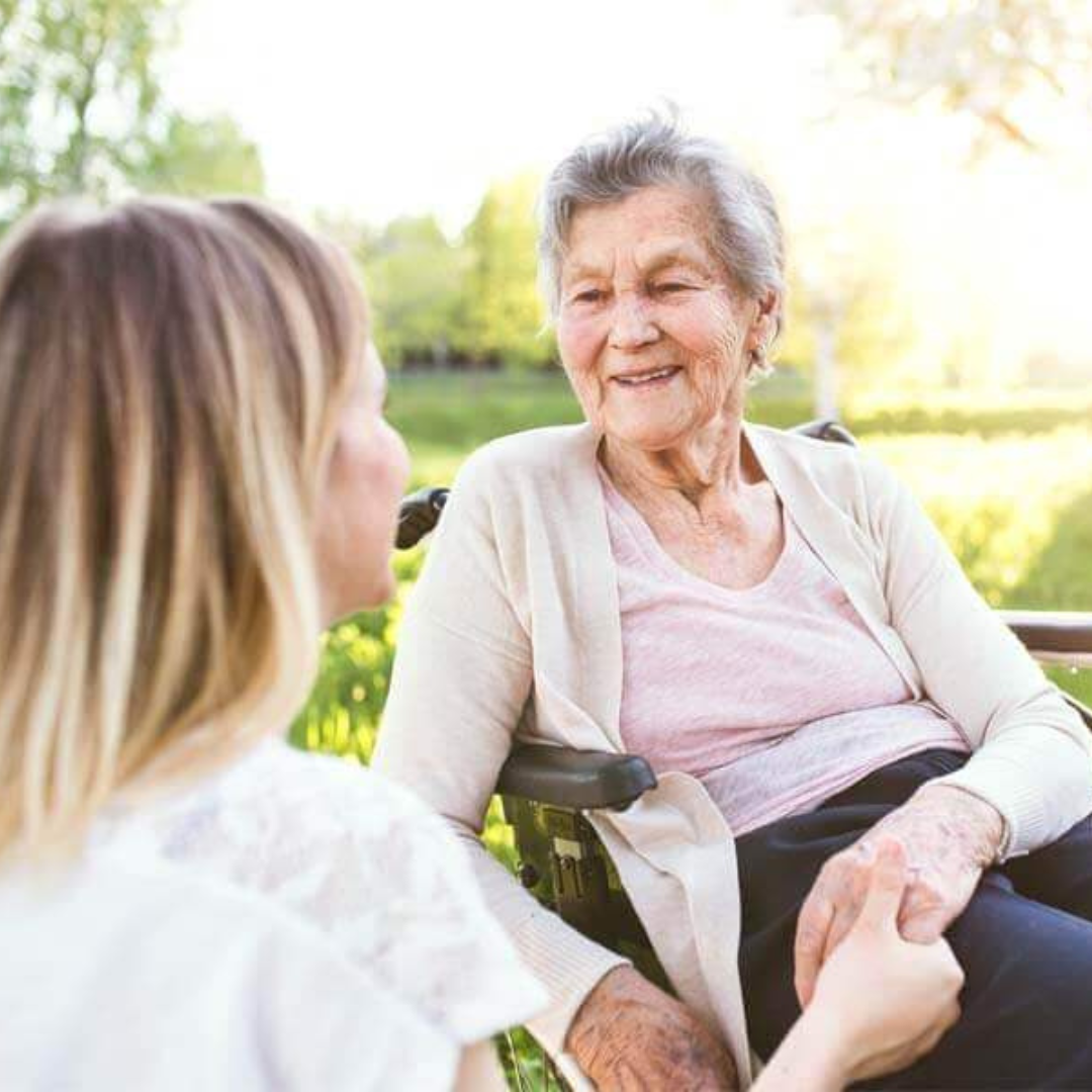 An elderly woman is sitting on a bench talking to a younger woman.