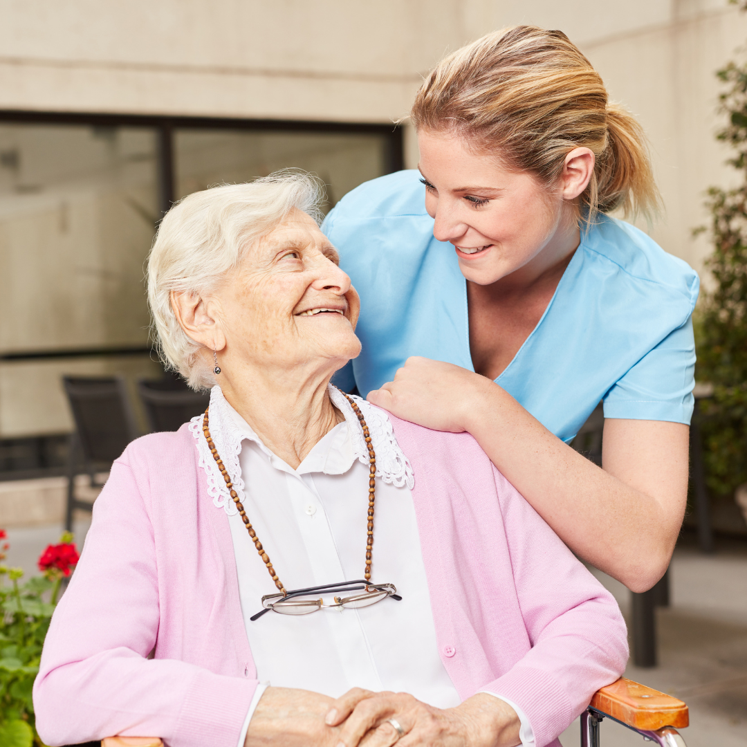 An elderly woman in a wheelchair is being helped by a nurse.