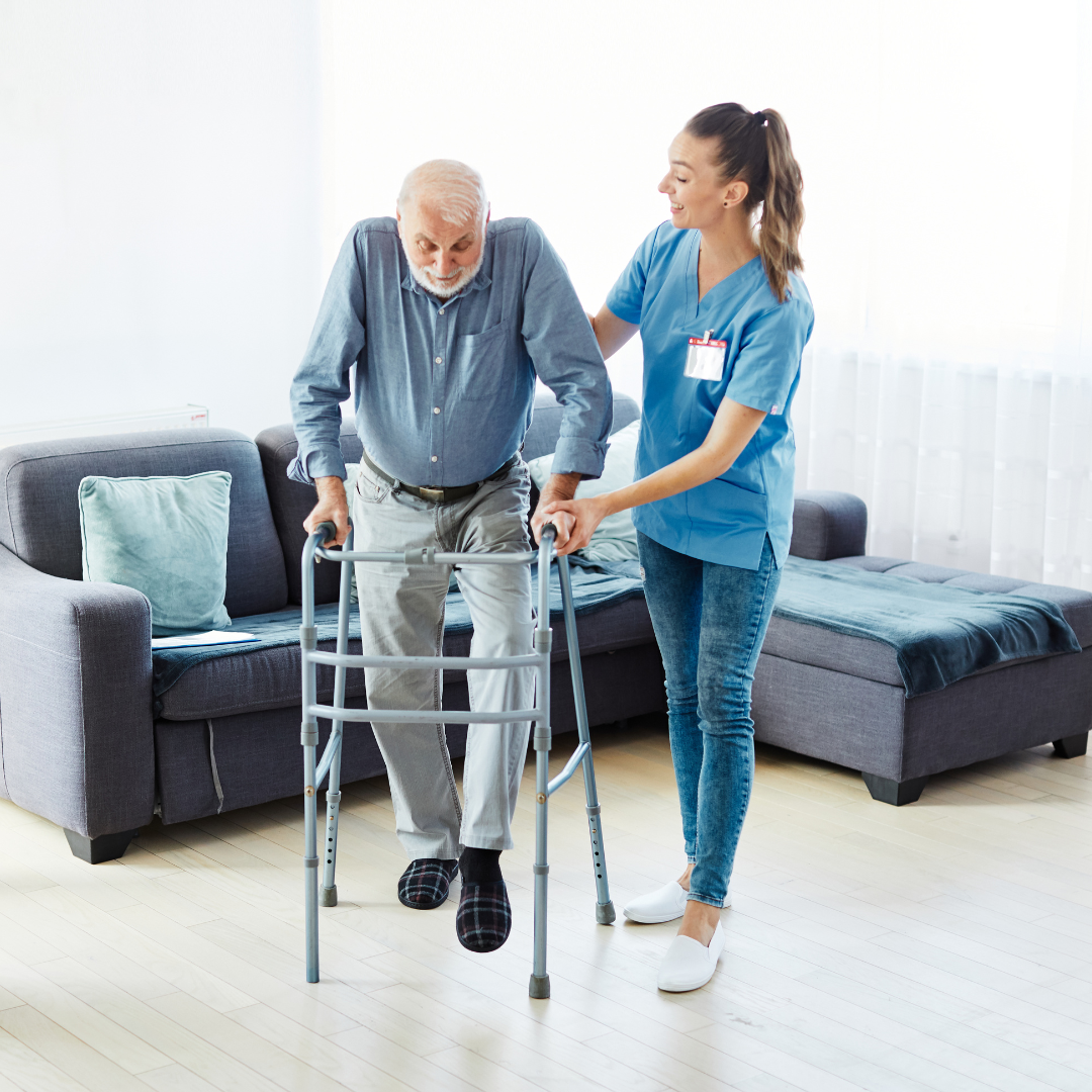 A nurse is helping an elderly man use a walker in a living room.