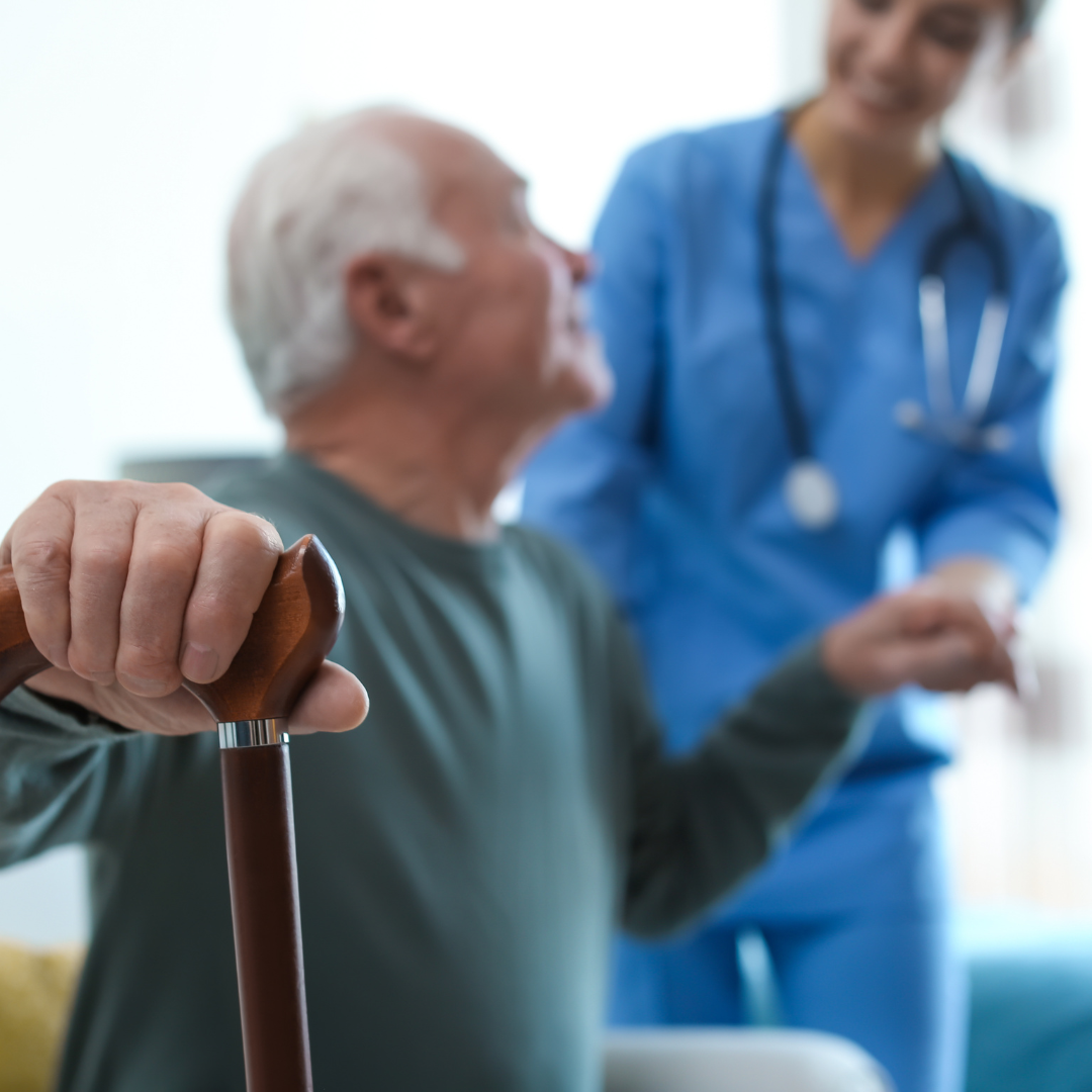 An elderly man with a cane is being helped by a nurse