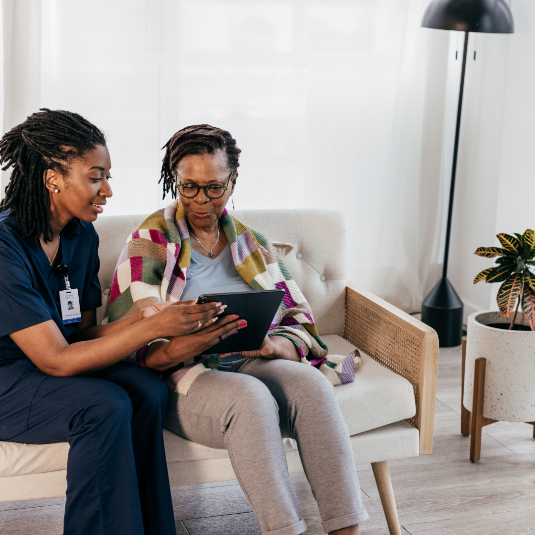 Two women are sitting on a couch looking at a tablet.