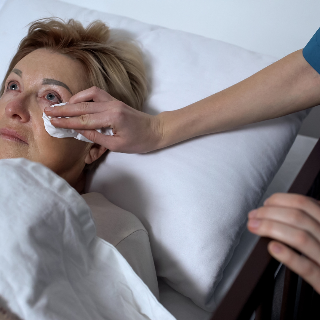 A woman is laying in a hospital bed while a person wipes her face with a napkin