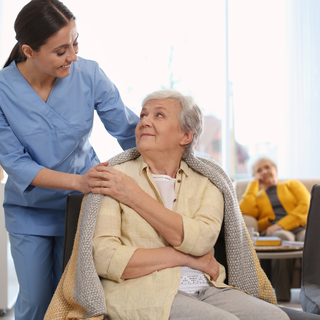 An elderly woman in a wheelchair is being helped by a nurse.