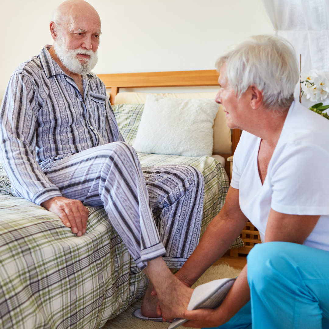 An elderly man is sitting on a bed talking to a nurse