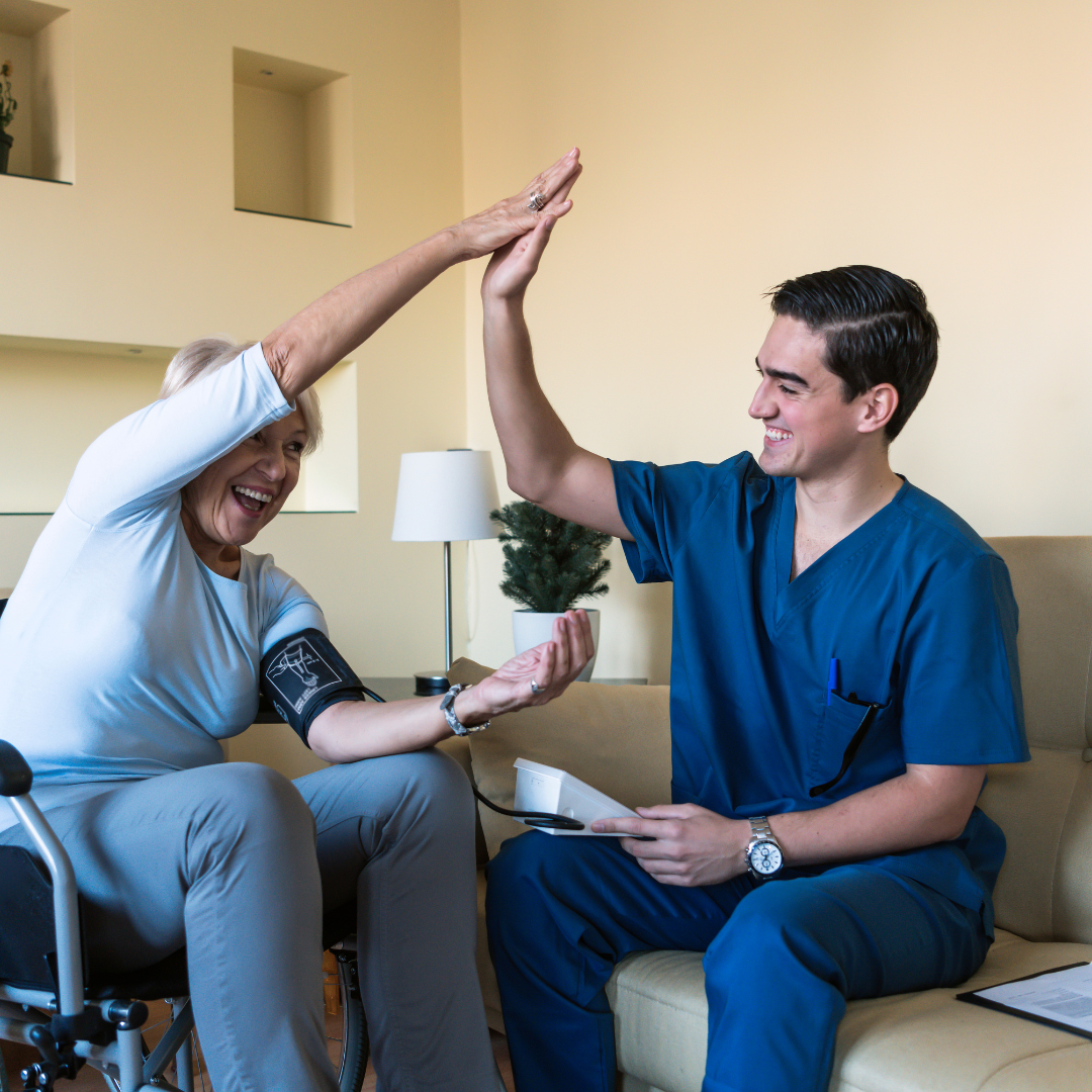 A man in a blue scrub is giving a woman in a wheelchair a high five.