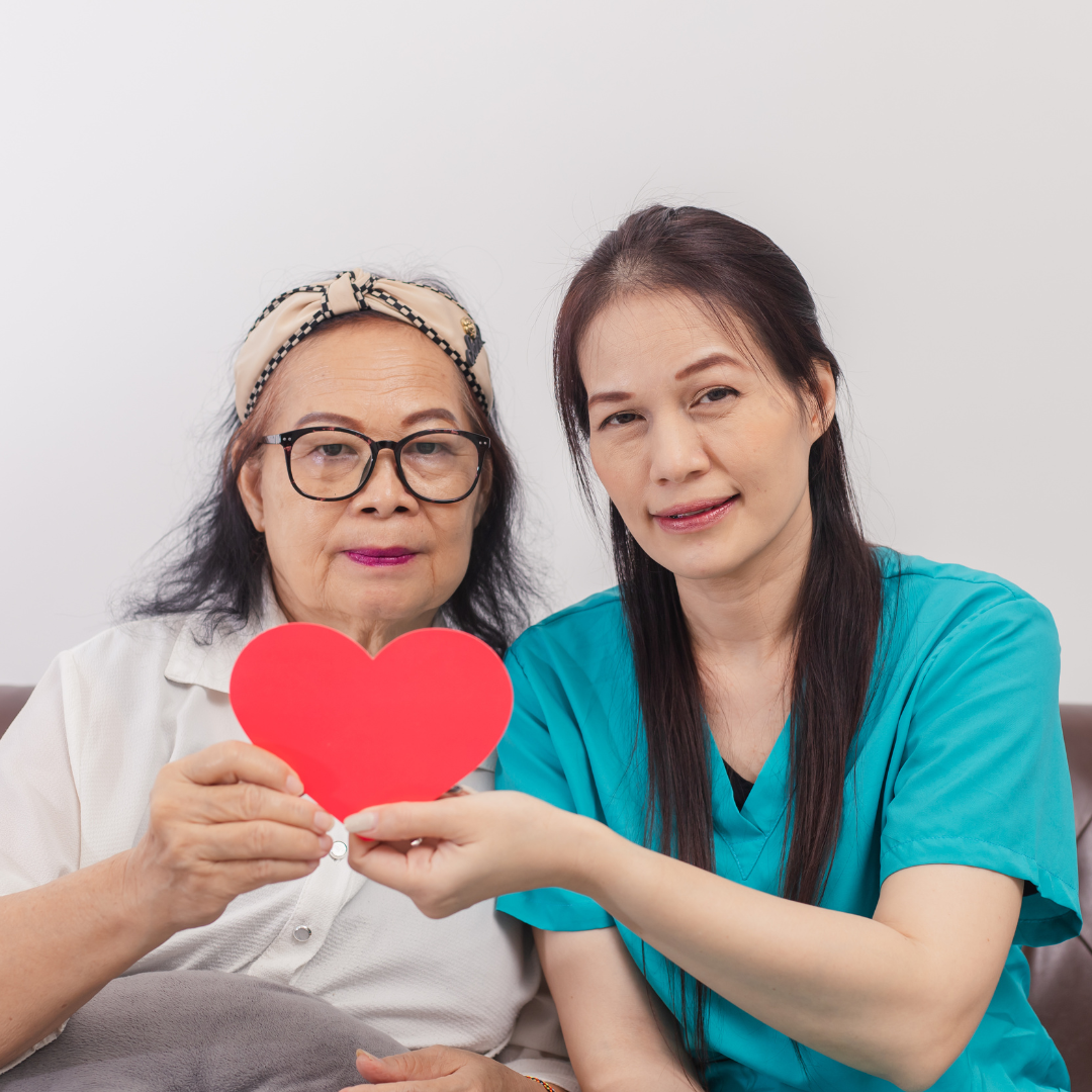 Two women are sitting on a couch holding a red heart