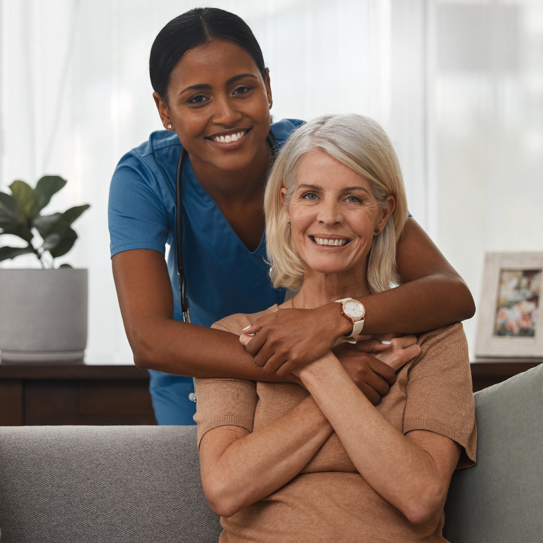 A nurse is hugging an older woman who is sitting on a couch.