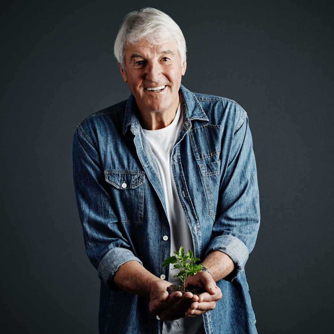 A man in a denim shirt is holding a small plant in his hands.