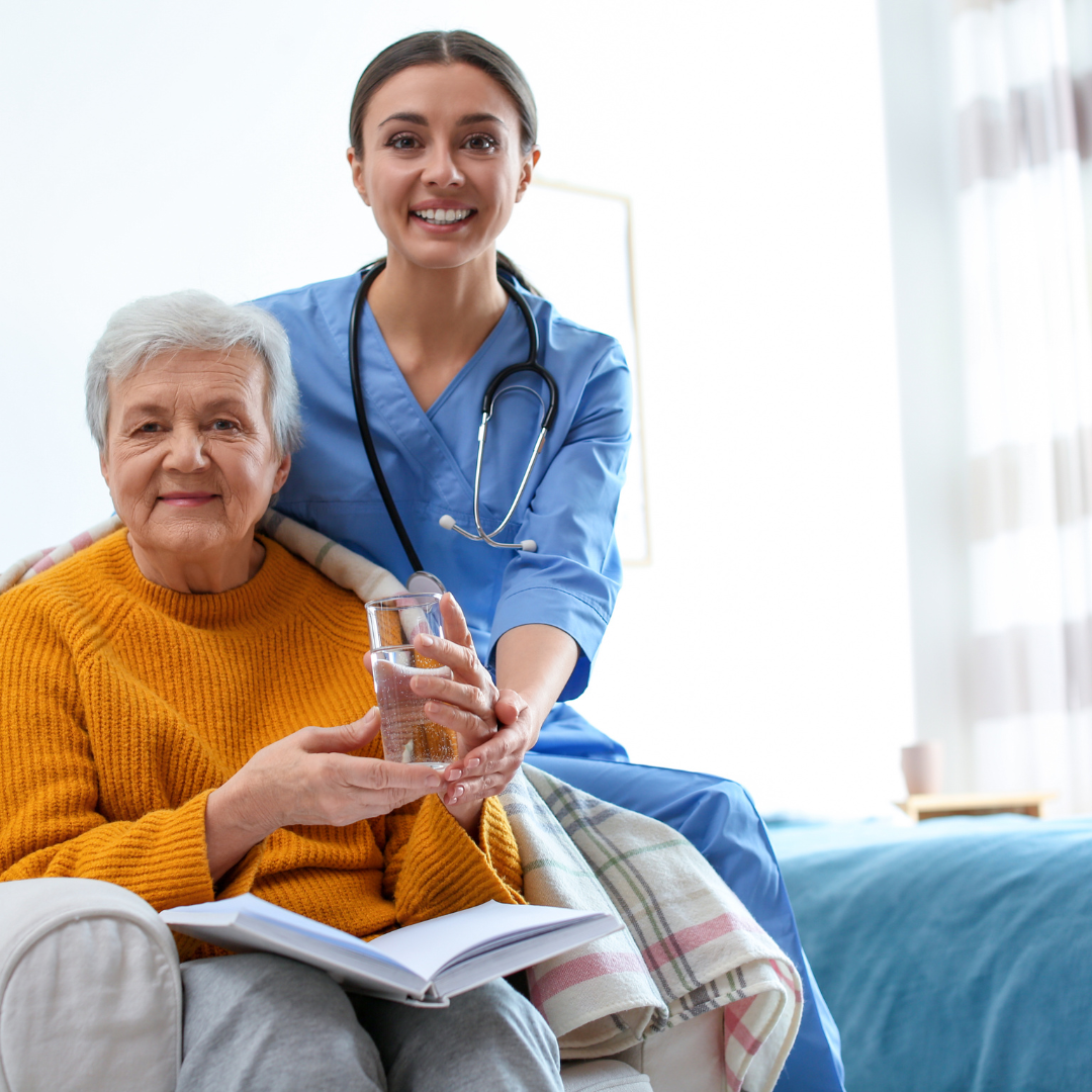 A nurse is sitting next to an elderly woman on a bed.