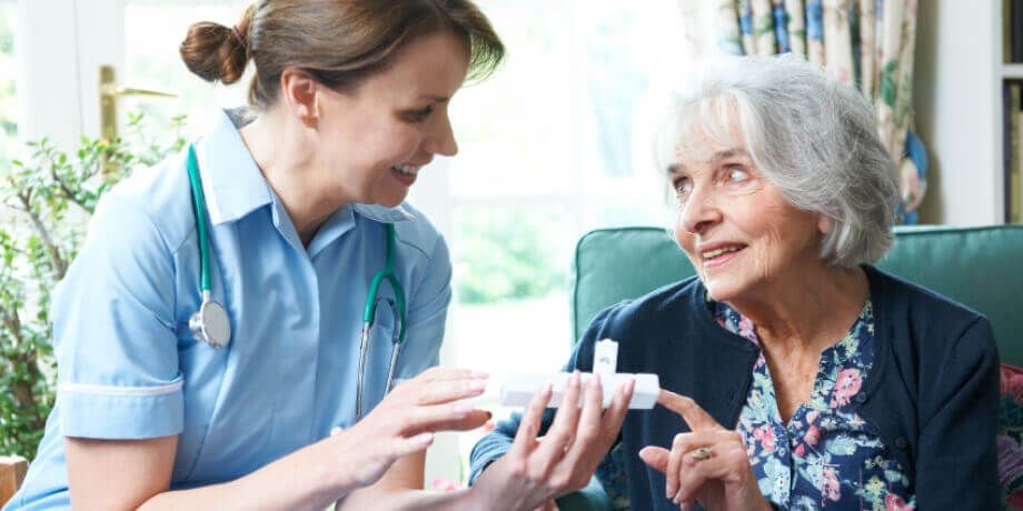 A nurse is talking to an elderly woman who is sitting on a couch.