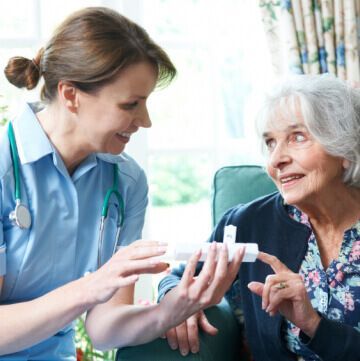 A nurse is talking to an elderly woman who is sitting on a couch.