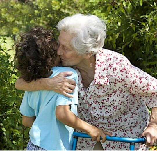 An elderly woman is giving her caregiver a hug outdoors.