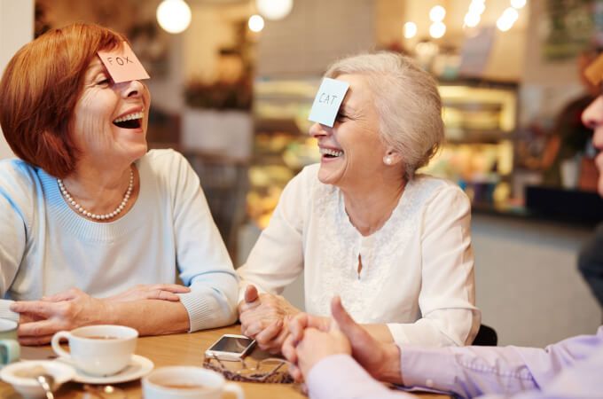 A group of older women are sitting at a table laughing and playing a game.