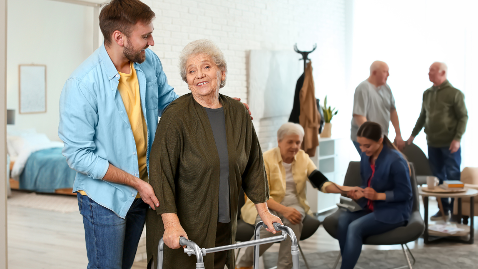 Care Worker Helping to Elderly Woman with Walker in Geriatric Ho