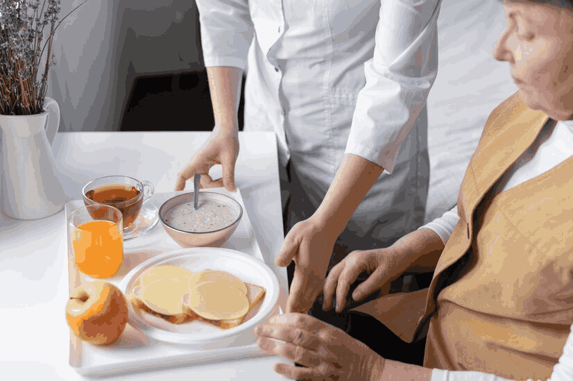 A woman is serving food to an elderly man in a wheelchair.