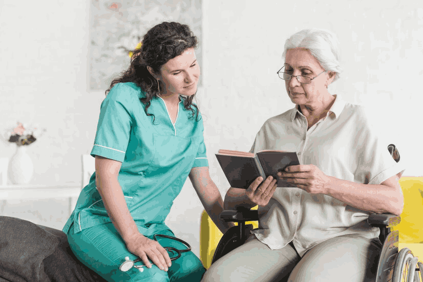 A nurse is sitting next to an elderly woman in a wheelchair.