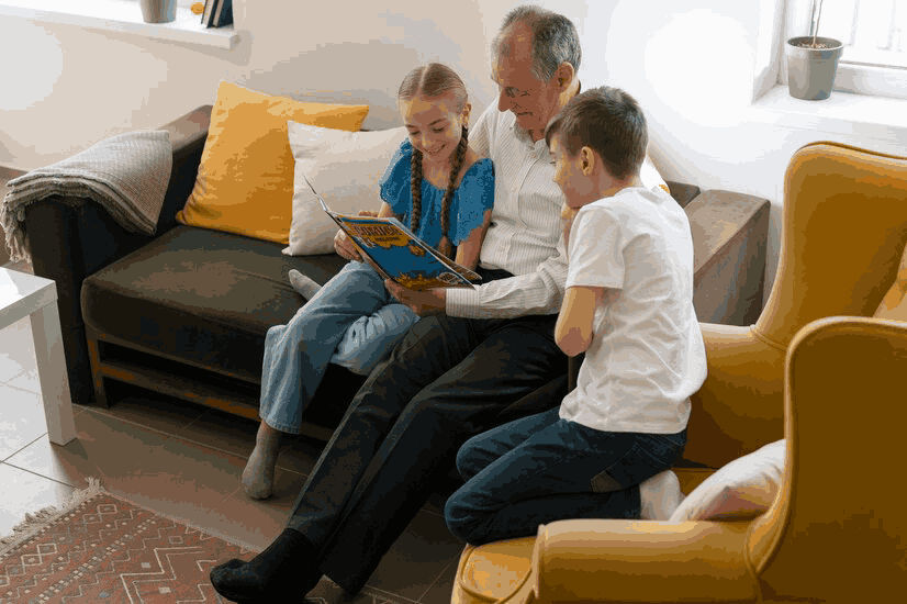 A man is sitting on a couch reading a book to two children.