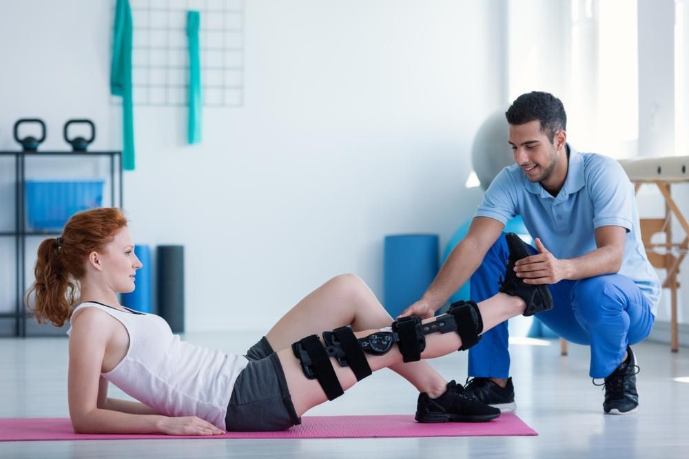 A Man Is Helping a Woman with A Knee Brace — Action Physiotherapy in Cooks Hill, NSW