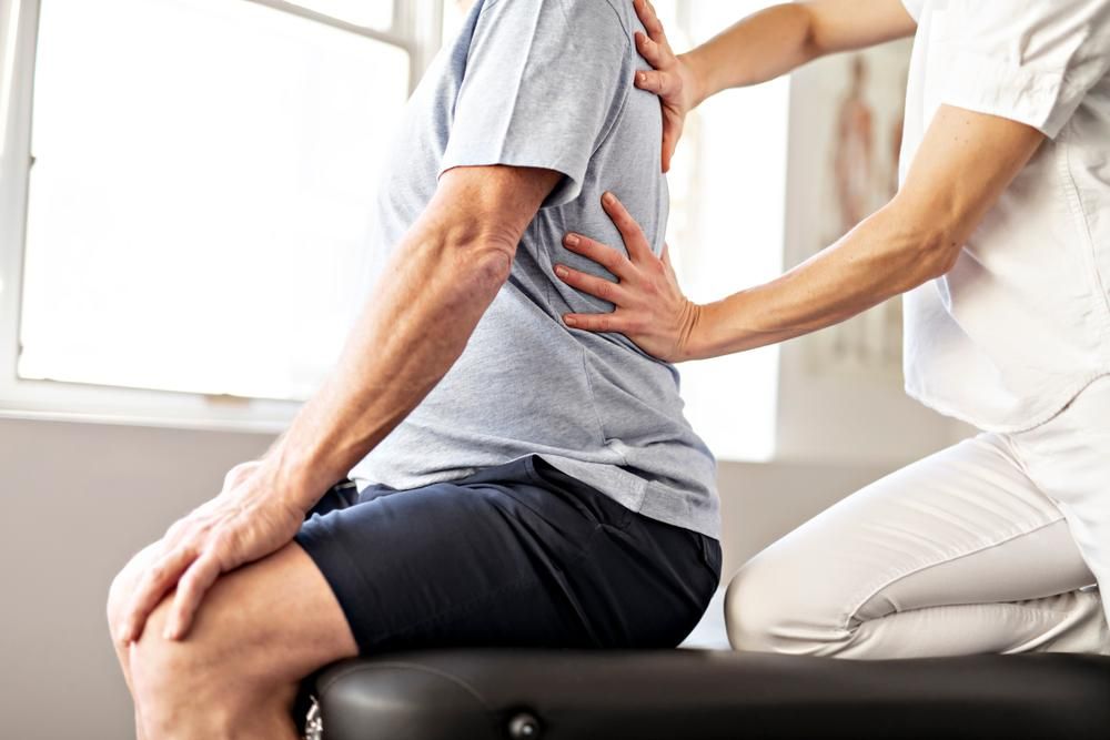 A Man Is Getting a Back Massage from A Nurse While Sitting on A Table — Action Physiotherapy in Cooks Hill, NSW