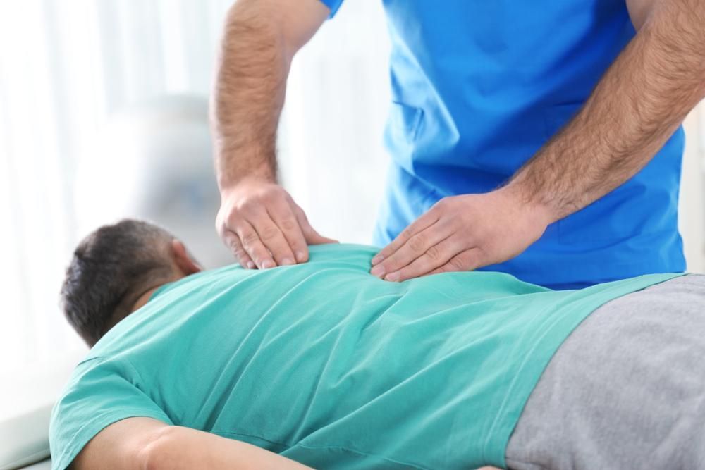 A Man Is Laying on A Bed Getting a Massage from A Doctor — Action Physiotherapy in Cooks Hill, NSW