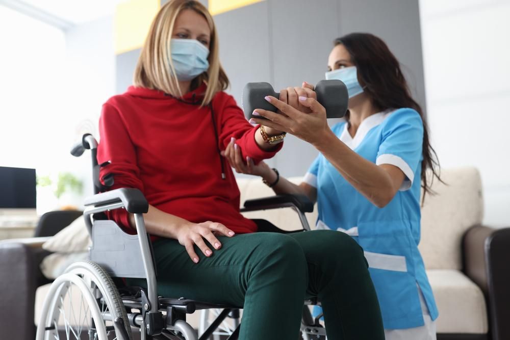 A Nurse Is Helping a Woman in A Wheelchair Lift a Dumbbell — Action Physiotherapy in Cooks Hill, NSW