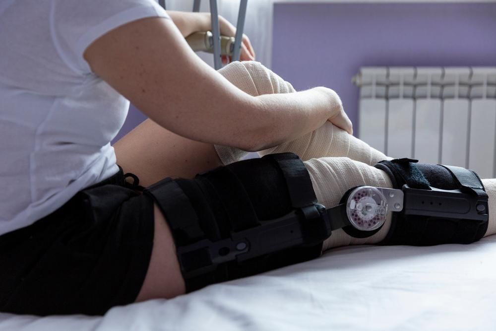 A Woman with A Knee Brace Is Sitting on A Bed — Action Physiotherapy in Cooks Hill, NSW