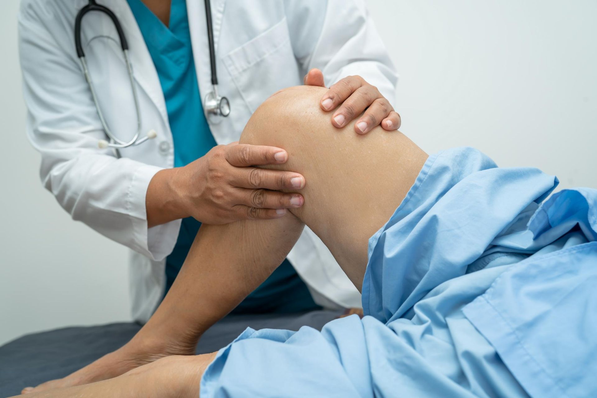 A Doctor Is Examining a Patient's Knee in A Hospital Bed — Action Physiotherapy in Cooks Hill, NSW