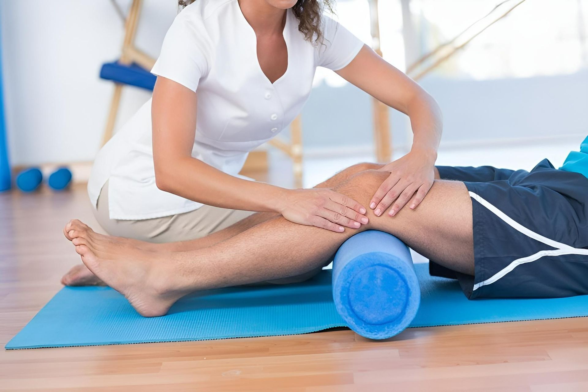 A Woman Is Massaging a Man's Leg with A Blue Foam Roller — Action Physiotherapy in Cooks Hill, NSW