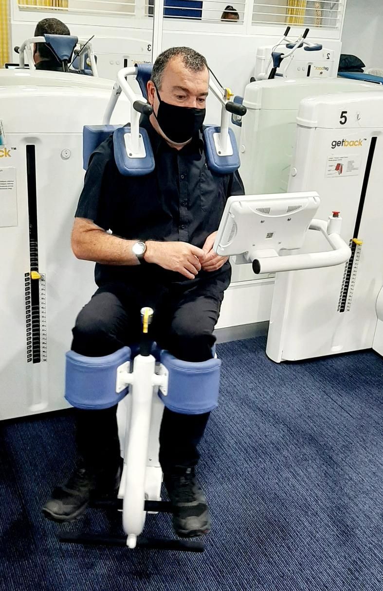 A Man Wearing a Mask Is Sitting on A Machine in A Gym — Action Physiotherapy in Cooks Hill, NSW