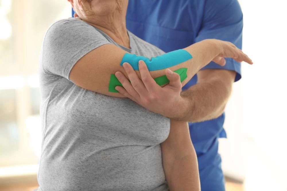 A Man Is Putting Kinesio Tape on A Woman's Elbow — Action Physiotherapy in Cooks Hill, NSW