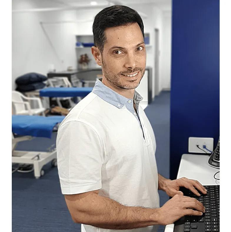 A Man in A White Shirt Is Typing on A Laptop Computer — Action Physiotherapy in Cooks Hill, NSW