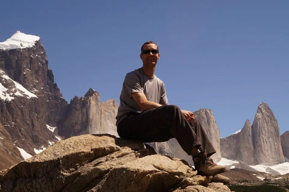 A Man Is Sitting on A Rock in Front of A Mountain — Action Physiotherapy in Cooks Hill, NSW