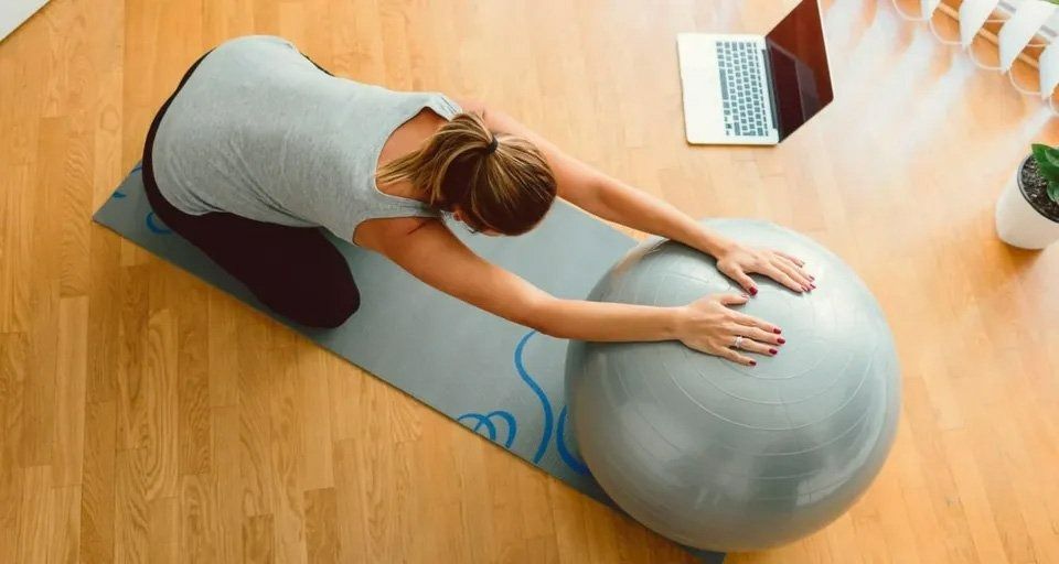 A Woman Is Stretching on A Yoga Mat Next to An Exercise Ball — Action Physiotherapy in Cooks Hill, NSW