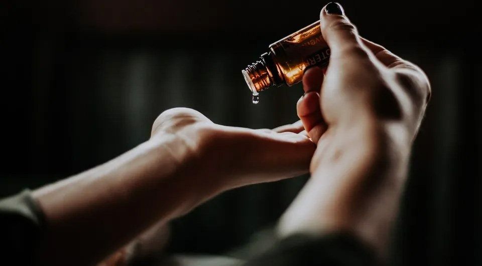 A Woman Is Pouring Essential Oil Into Her Hand — Action Physiotherapy in Cooks Hill, NSW