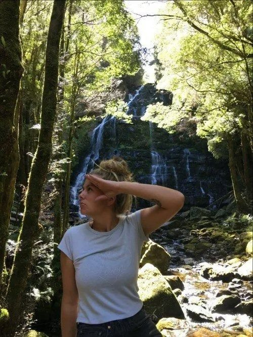 A Woman Is Standing in Front of A Waterfall in The Woods — Action Physiotherapy in Cooks Hill, NSW