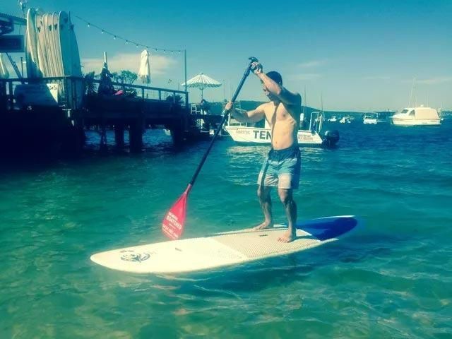 A Man Is Standing on A Paddle Board in The Water — Action Physiotherapy in Cooks Hill, NSW