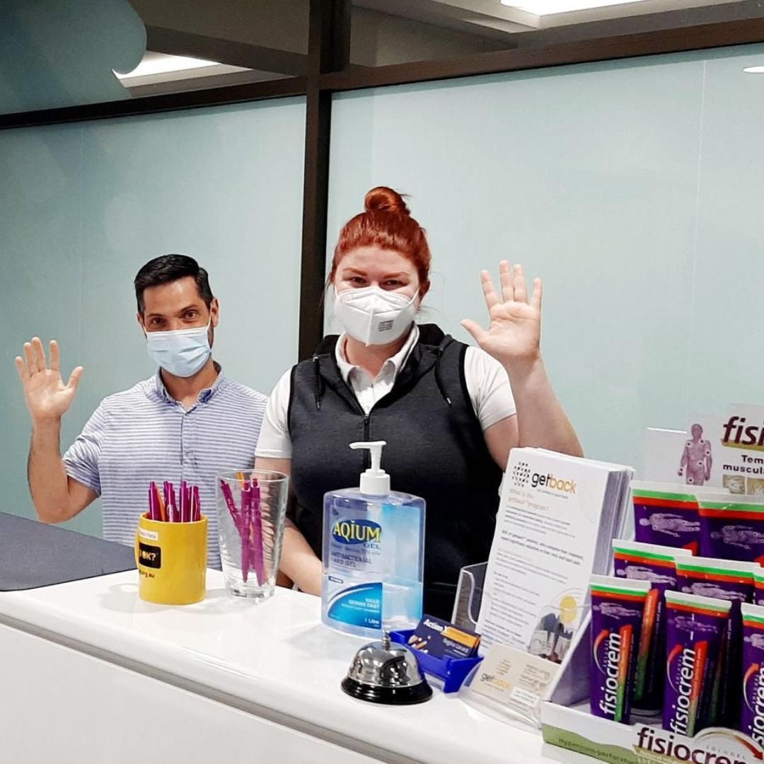 A Man and A Woman Wearing Masks Are Standing at A Counter — Action Physiotherapy in Cooks Hill, NSW