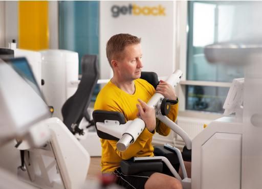 A Man in A Yellow Shirt Is Sitting on A Machine in A Gym — Action Physiotherapy in Cooks Hill, NSW