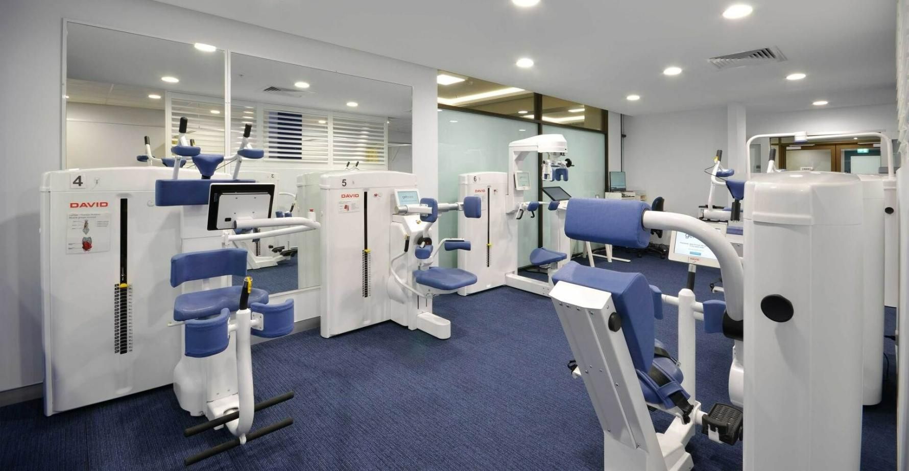 A Gym with A Lot of Exercise Equipment and A Blue Carpet — Action Physiotherapy in Cooks Hill, NSW