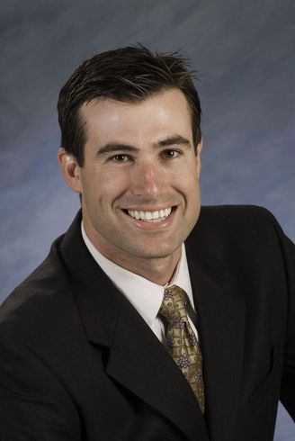 A person points to a document on a table while another holds a small model house, representing a real estate meeting.