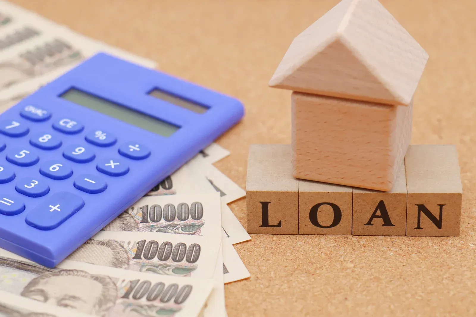 Two people discuss a property purchase, with a model house and a calculator on a desk with paperwork.