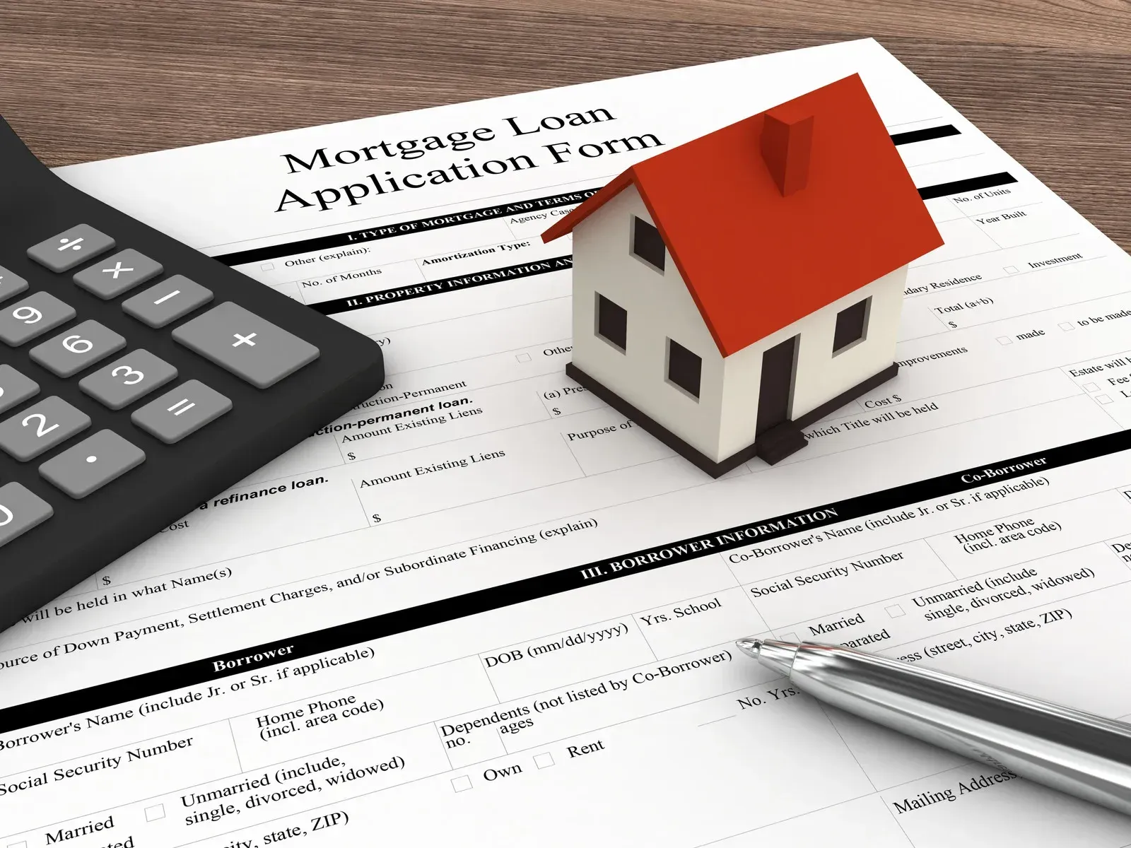 A model house, a calculator, and a pen rest on top of a mortgage loan application form.