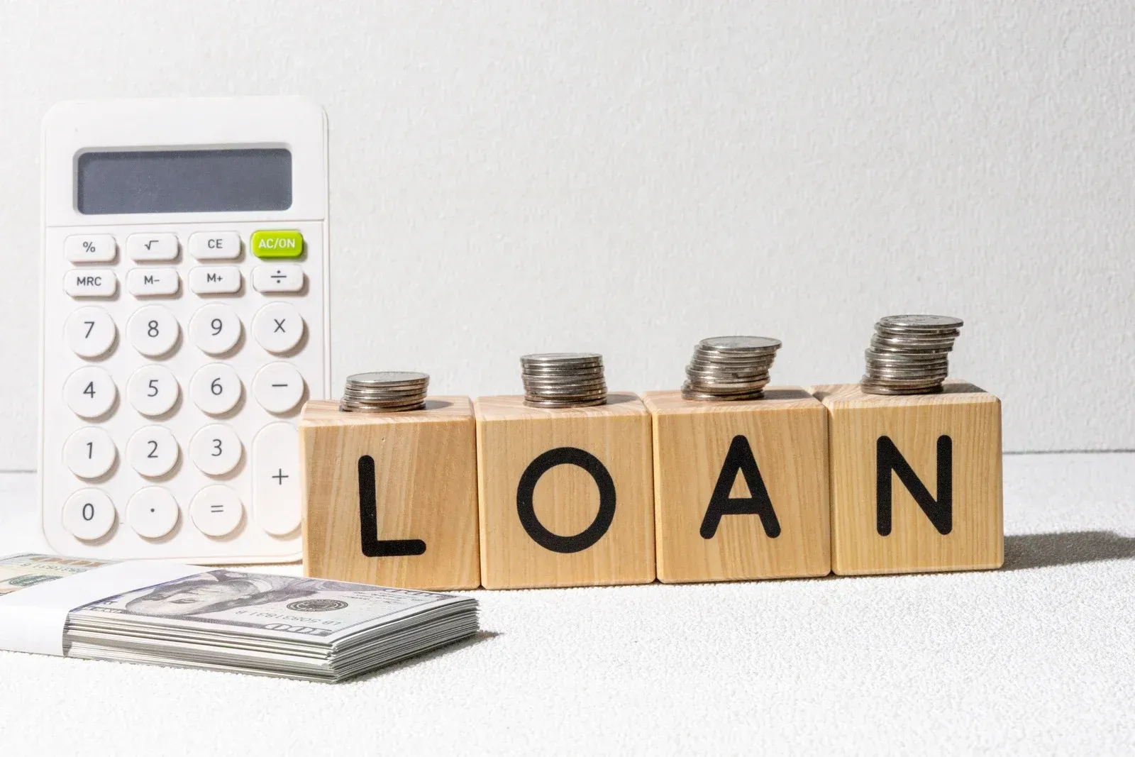 A calculator, a stack of cash, and wooden blocks spelling 