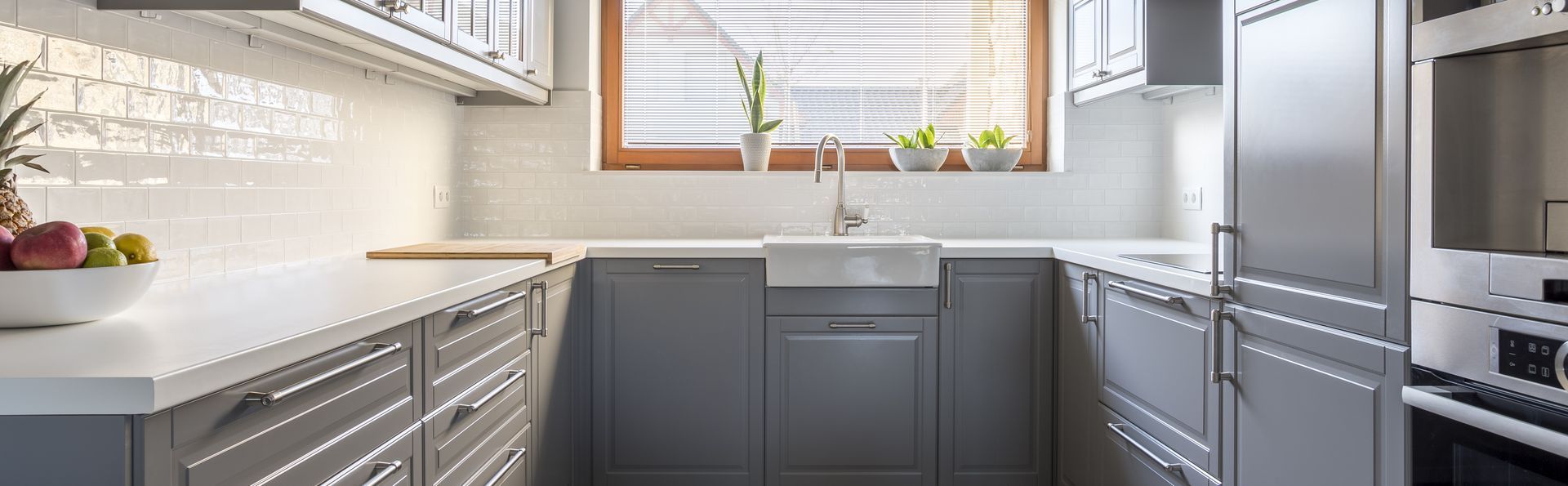 A gray kitchen with white countertops and backsplash. A window is above the sink.