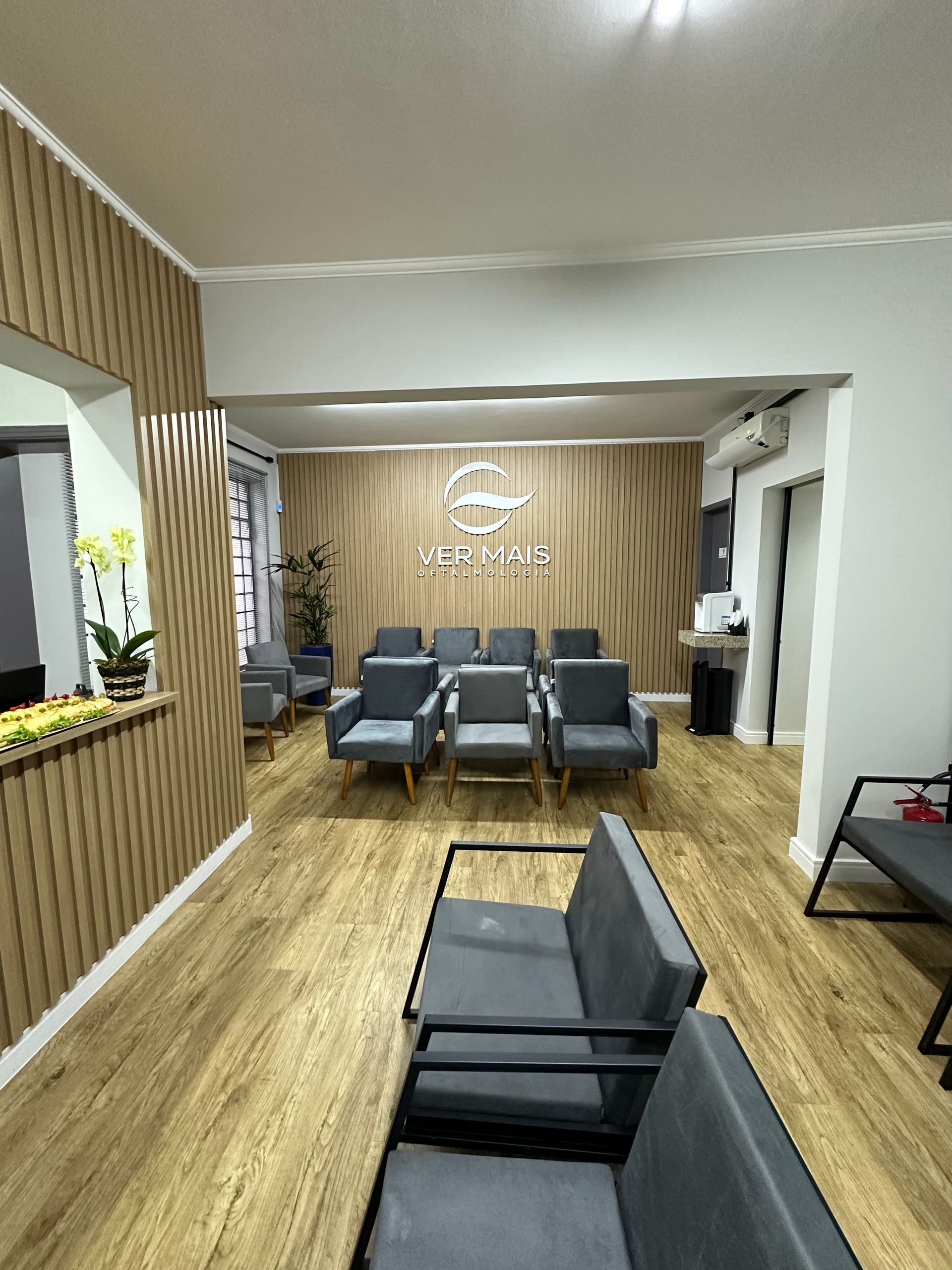Sala de espera com cadeiras cinzentas, painéis de madeira e um logotipo na parede do fundo.