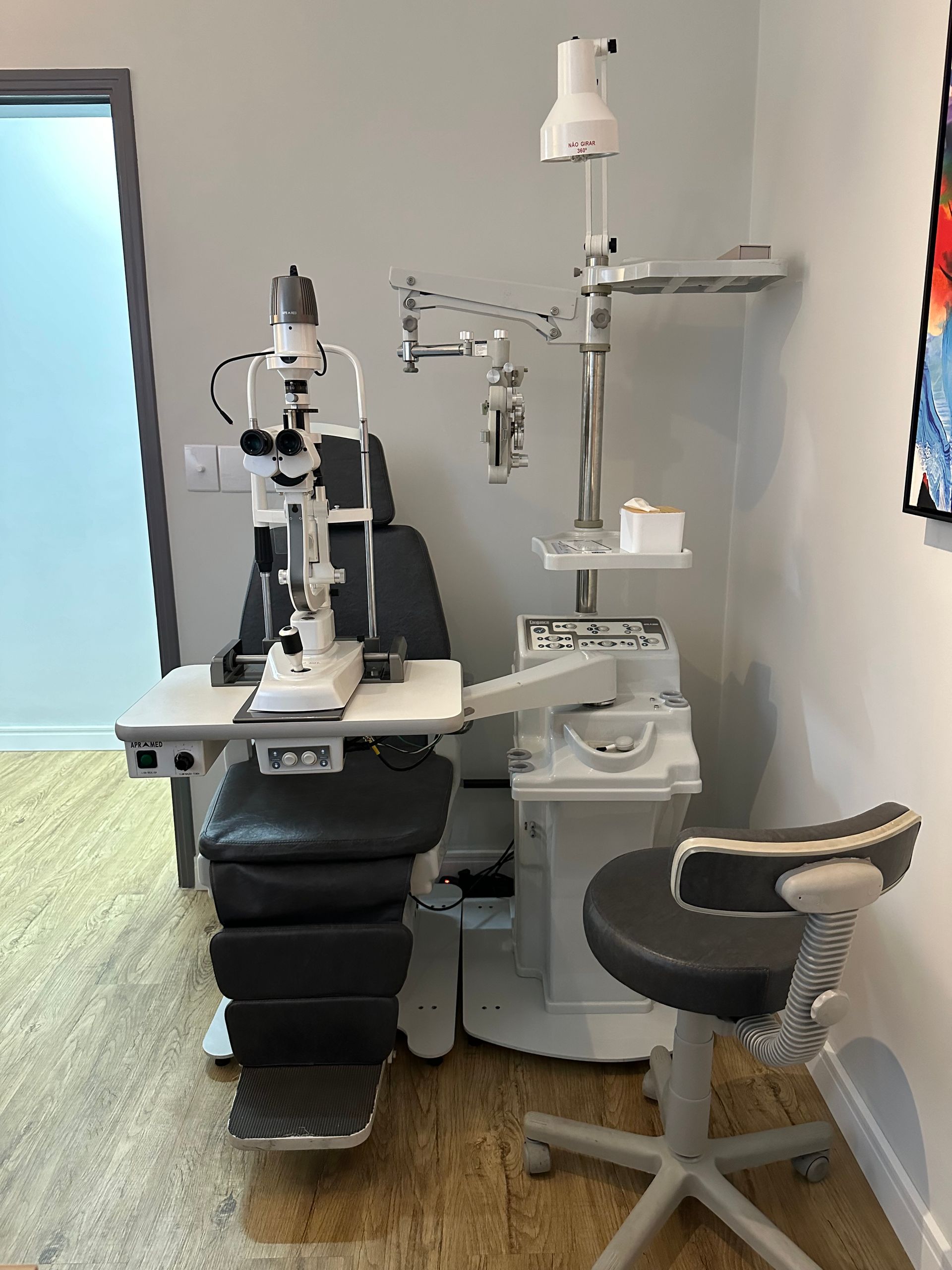 Consultório oftalmológico com cadeira, lâmpada de fenda e outros equipamentos médicos.