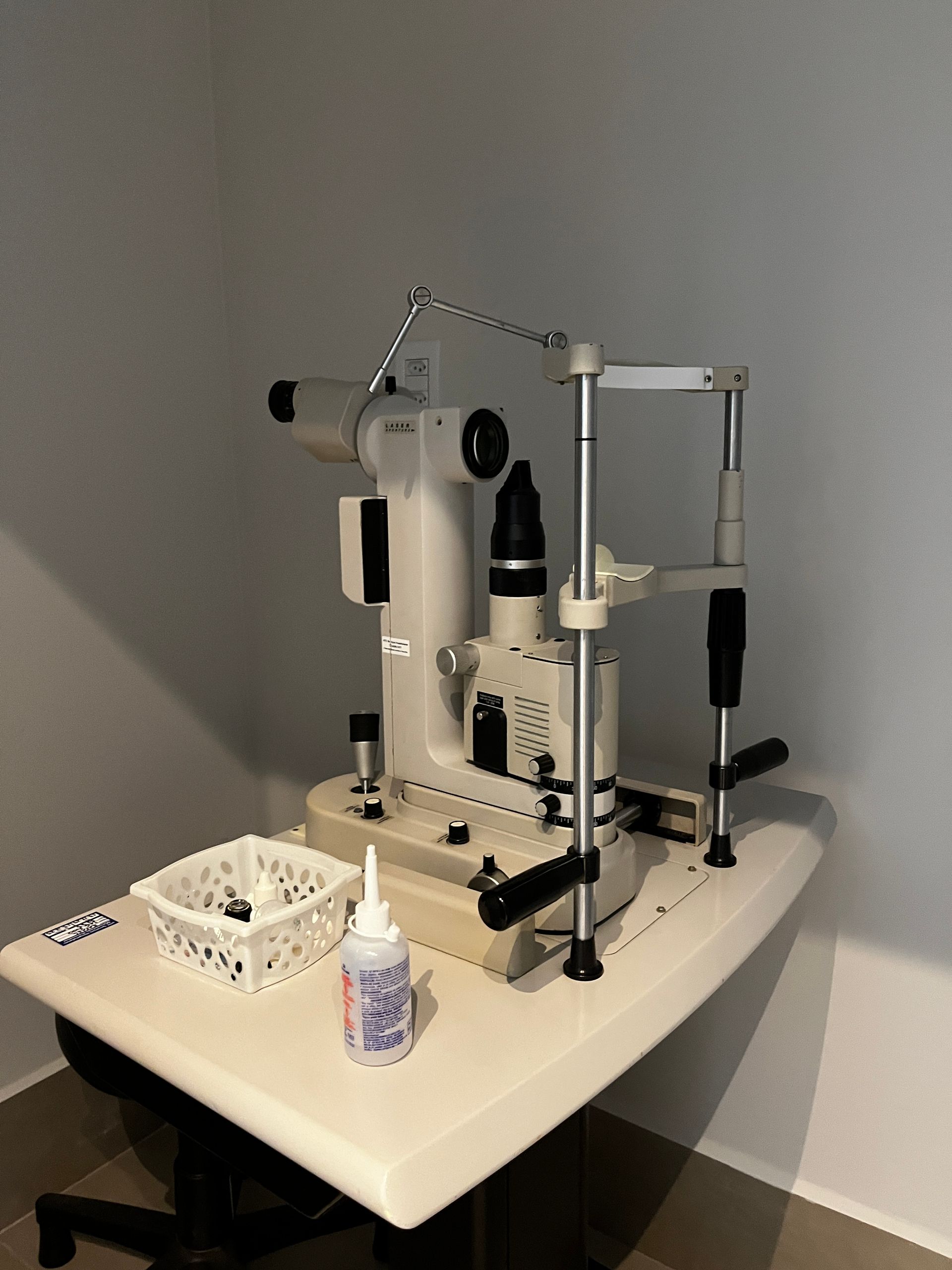 Biomicroscópio de lâmpada de fenda sobre uma mesa em um ambiente clínico; equipamento médico em preto e branco.