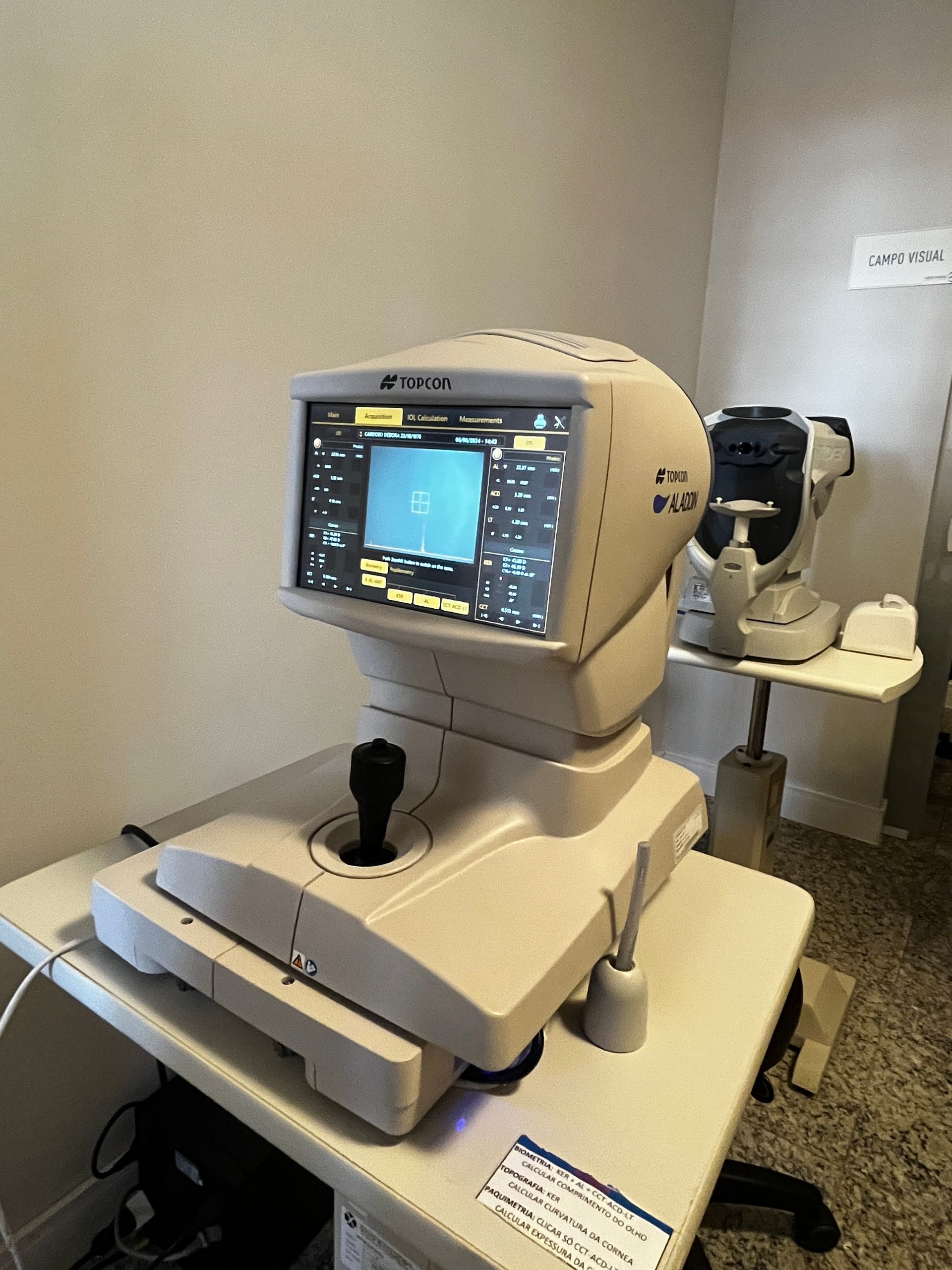 Uma máquina de exame oftalmológico com tela e joystick. Outro aparelho semelhante está localizado atrás dela.